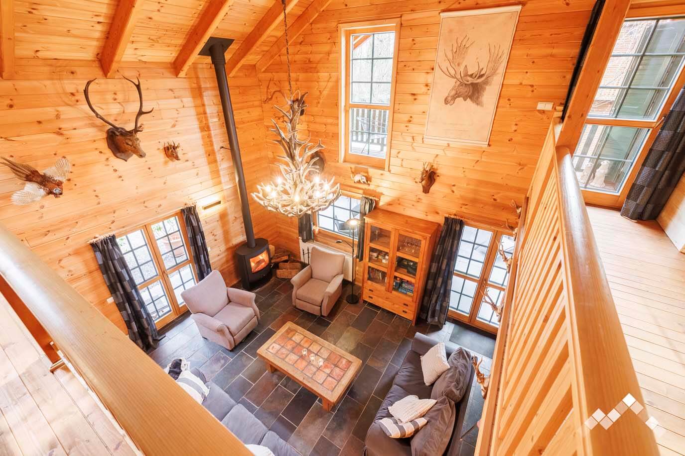 Vue plongeante sur le salon spacieux du chalet avec sa haute charpente en bois et son ambiance montagne.